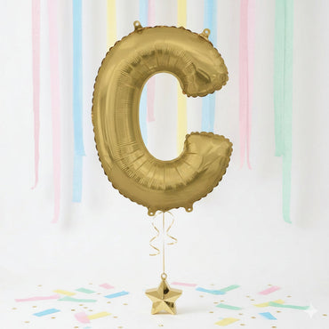 Gold letter 'C' balloon with a star-shaped weight against a pastel striped background - Party Centre