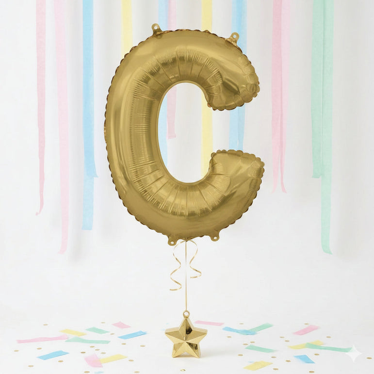 Gold letter 'C' balloon with a star-shaped weight against a pastel striped background