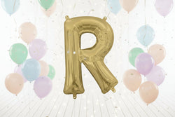 Gold letter 'R' balloon against a white curtain background