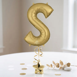 Gold letter 'S' balloon with decorative elements on a light surface
