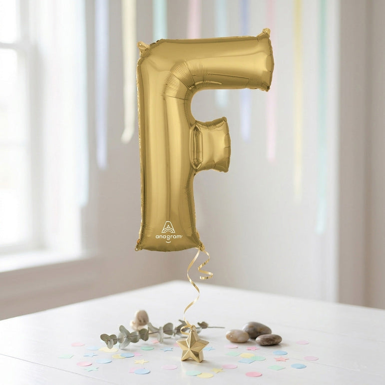 Gold letter 'F' balloon on a white surface with confetti and decorative elements.