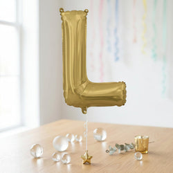 Gold letter 'L' balloon on a wooden surface with decorative items.