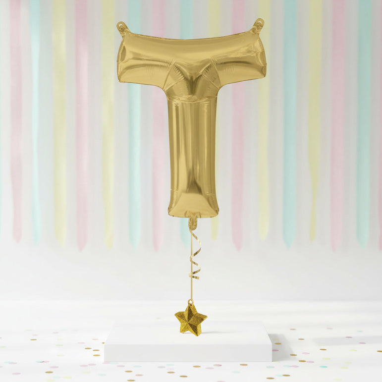 Gold foil balloon shaped like a letter 'T' with a star on a pastel striped background